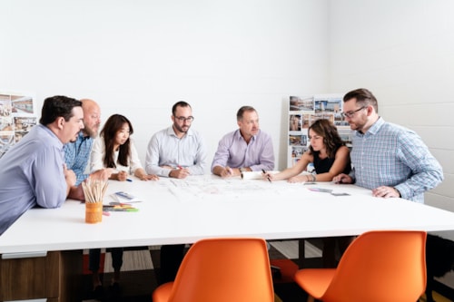 ALW employees sitting in orange chairs around table in a white meeting room, discussing a document